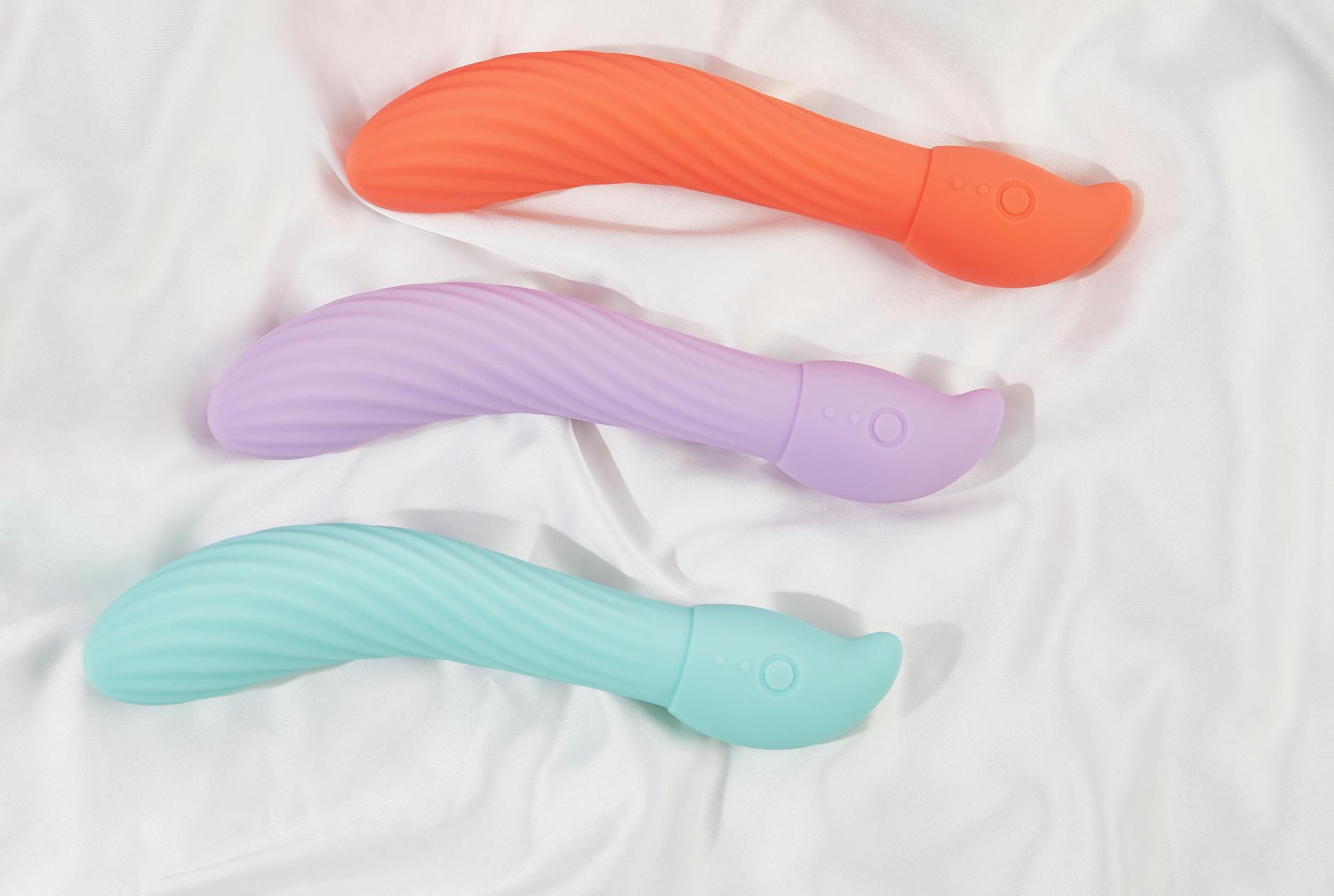 Três vibradores coloridos de silicone arranjados em tecido branco, destacando sua textura lisa e design moderno