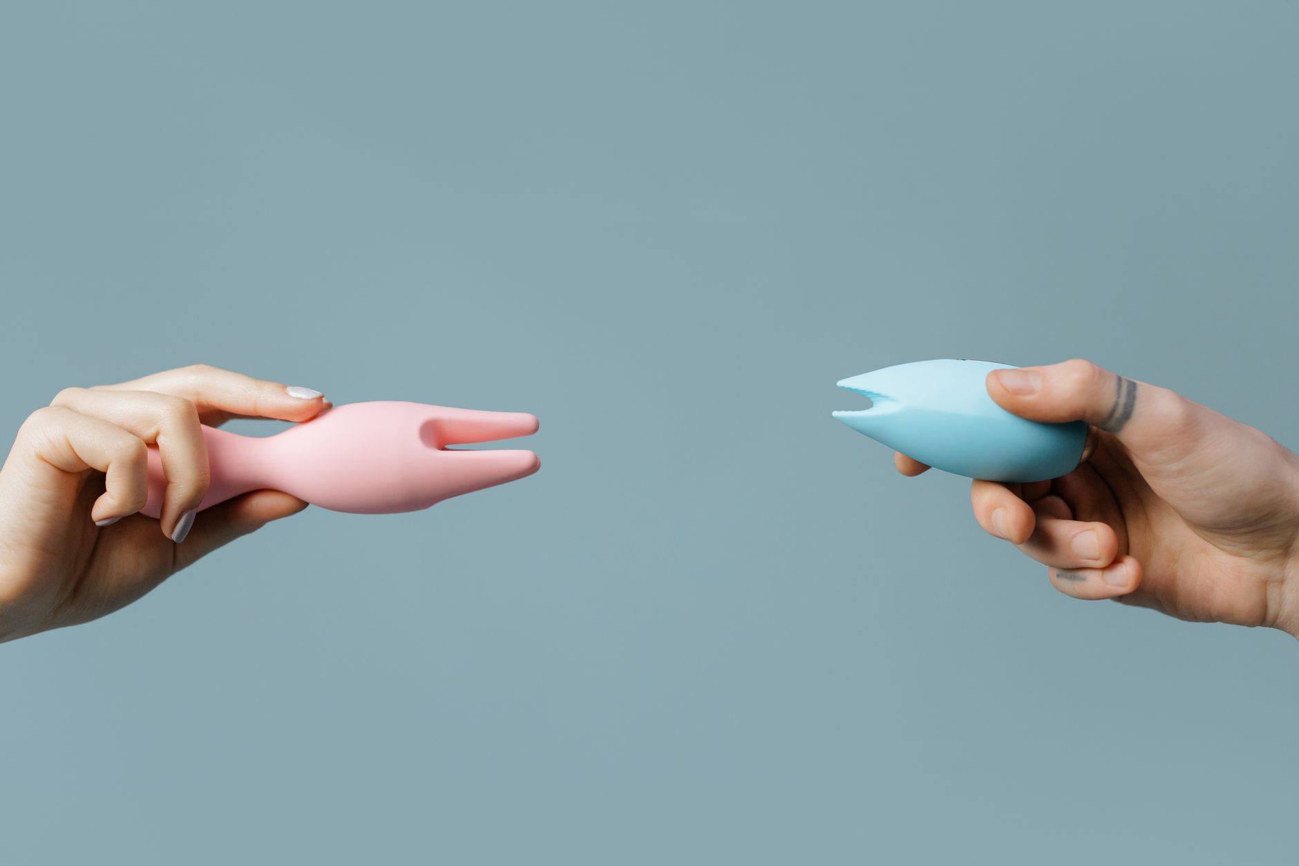 Photo of two hands holding colorful vibrators against a pastel background